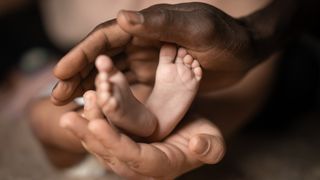 An adult holds a baby's feet in their hands